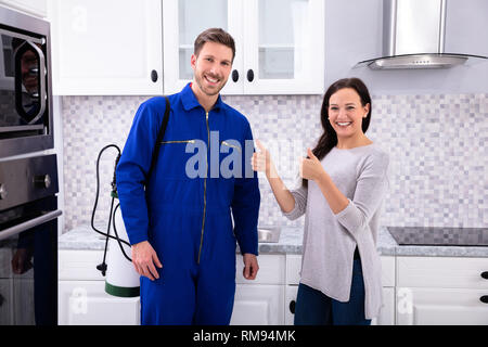 Woman Showing Thumbs Up With Pest Control Worker Standing In Kitchen Stock Photo