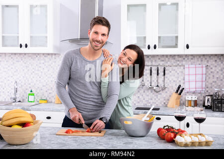 Front View Of Man With His Wife Cutting Vegetable On Chopping Board At Kitchen Worktop Stock Photo