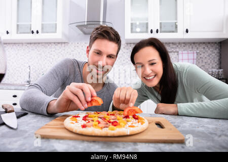 Portrait Of Happy Couple Preparing Pizza In Kitchen Stock Photo