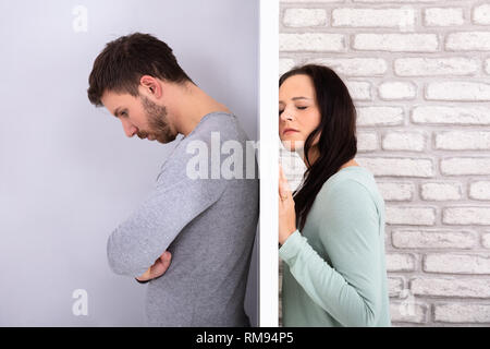 Side View Of Young Unhappy Couple Standing Back To Back At Home Stock Photo