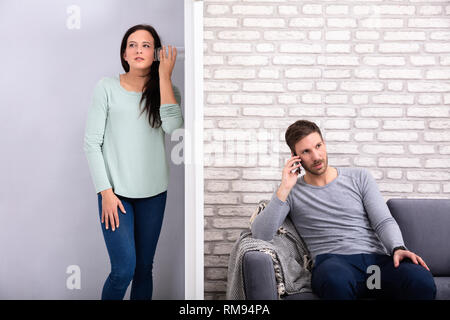Woman Standing Behind Glass Listening Neighbor Man's Conversation Sitting On Sofa Stock Photo