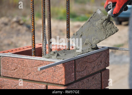 Bricklayer hand laying brick column with metal rod Stock Photo
