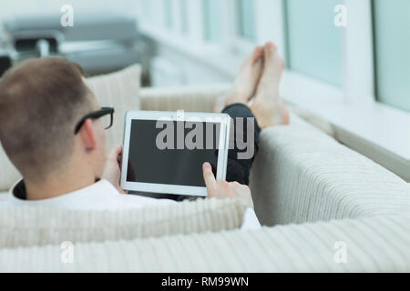 rear view.a young man with a digital tablet sitting on a couch in his living room Stock Photo