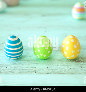 Three colorful Easter eggs decorated with stripes, flowers and spots in blue, green and yellow on green wood background with copy space for your holid Stock Photo