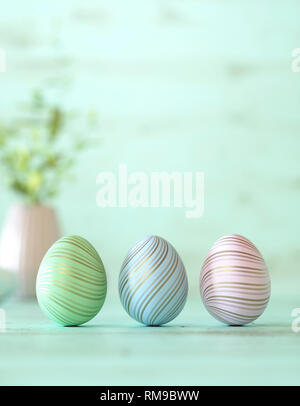 Beautiful Easter eggs decorated in blue, green and pink colors, balanced vertically on its blunt end on cyan background with copy space for your holid Stock Photo