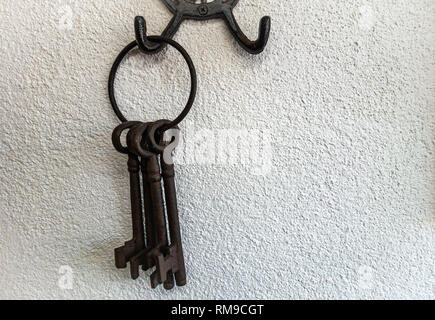 Large Old iron metal keys hanging on a hook on a plain white wall Stock Photo