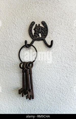 Large Old iron metal keys hanging on a hook on a plain white wall Stock Photo