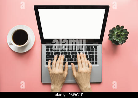 Woman typing by laptop on office pink table. Top view with space for text on screen. Stock Photo