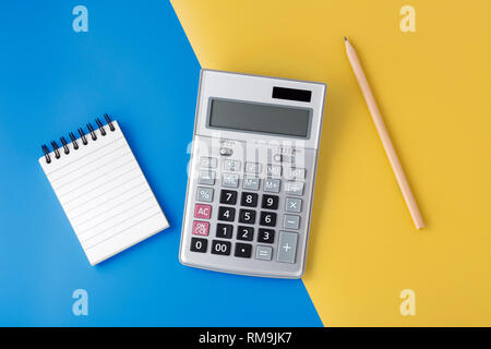 Sliver calculator on yellow and blue background with notepad and pencil, flat lay with space Stock Photo