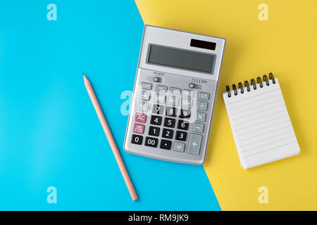 Calculator on light blue and yellow background with notepad and pencil, flat lay with space Stock Photo