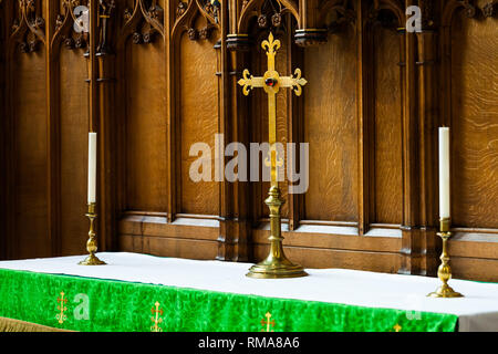 BIRMINGHAM, UK - March 2018 Celtic Cross and Candlestick Holder Made of Brass Standing on Altar Counter. Elaborate Wood Carving Details on Wall Panel. Stock Photo
