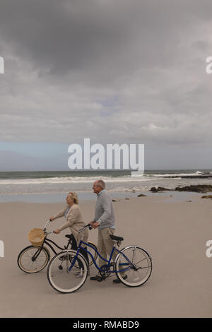 Happy senior couple walking with bicycle at the beach Stock Photo