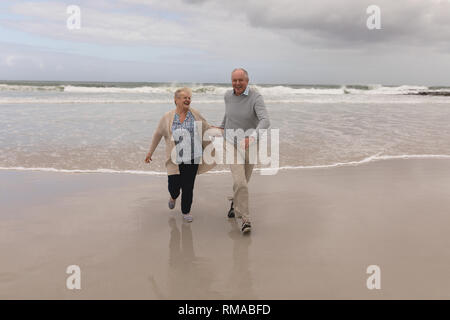 Senior couple running hand in hand on the beach Stock Photo
