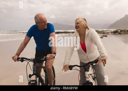 Senior couple riding a bicycle in a good mood on the beach Stock Photo