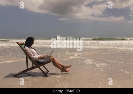 Young woman relaxing on sun lounger and using laptop Stock Photo