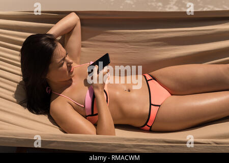 Young woman talking on mobile phone while relaxing on hammock Stock Photo