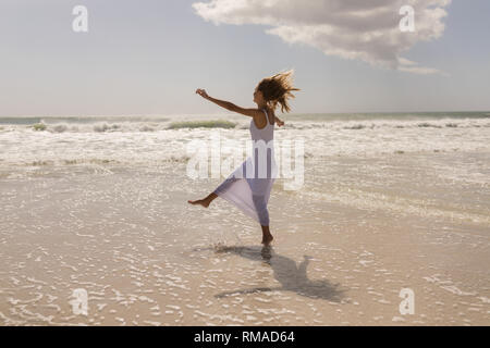 Beautiful happy young woman kicking water on beach Stock Photo