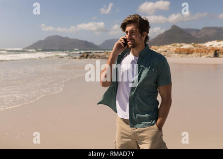 Young man with hand in pocket talking on mobile phone on beach Stock Photo