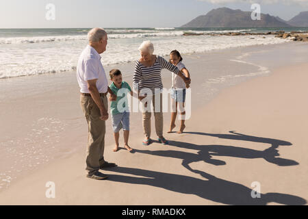 Happy multi-generation family holding hands and having fun on beach Stock Photo