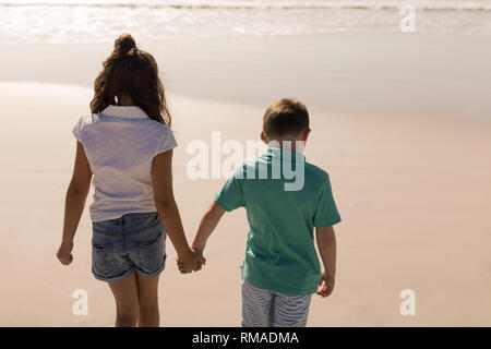 Siblings holding hands and walking on beach Stock Photo