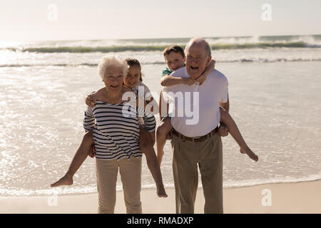 Happy grandparents giving piggyback to grandchildren on beach Stock Photo