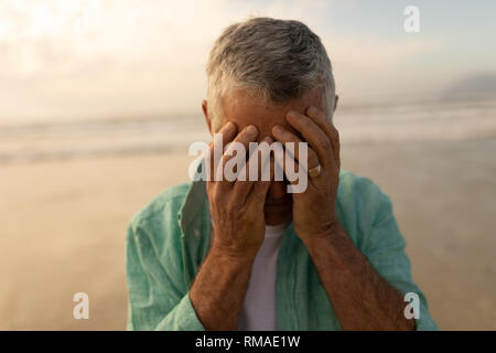 Senior man covering his face while standing on the beach Stock Photo