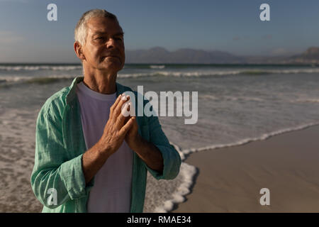 Senior man praying with eyes closed on the beach Stock Photo
