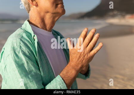 Senior man praying with eyes closed on the beach Stock Photo