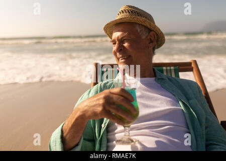 Senior man having cocktail drink while relaxing on sun lounger at beach Stock Photo