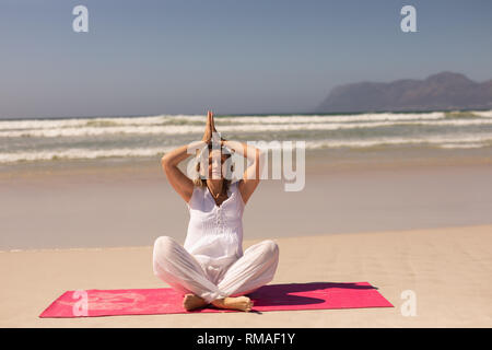 Front view of senior woman meditating in prayer position at beach Stock Photo