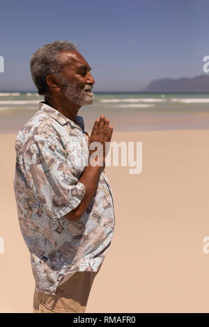 Senior black man with hands clasped praying on beach Stock Photo