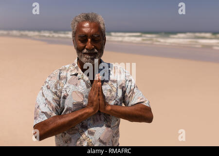 Senior black man with hands clasped praying on beach Stock Photo