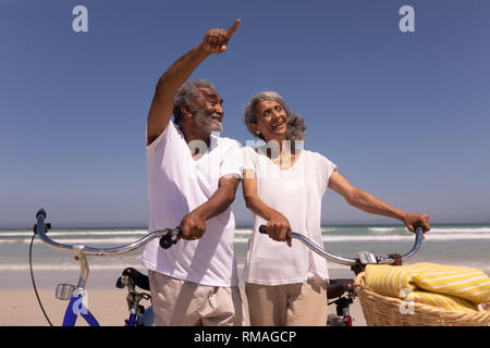 Senior man with bicycle pointing at distance on beach Stock Photo
