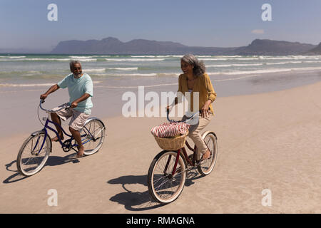 Senior couple riding bicycle on beach with mountains in the background Stock Photo