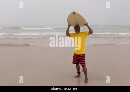 Senior male surfer carrying the surfboard on his head at beach Stock Photo