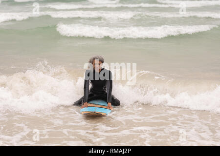 Senior female surfer sitting on surfboard in sea Stock Photo
