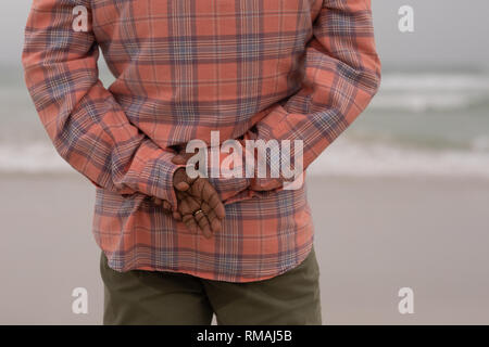 Senior man with hands behind back standing on the beach Stock Photo