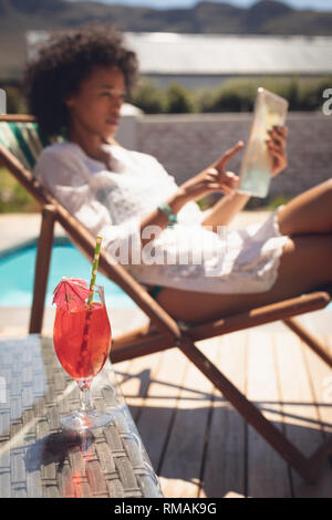 Glass of cocktail on table while woman using digital tablet in background Stock Photo