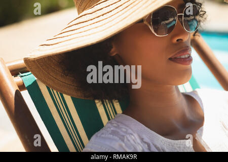 African American woman with hat and sunglasses relaxing on sun lounger in her backyard Stock Photo