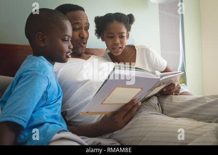 African American father with his children reading a storybook on bed in bedroom Stock Photo
