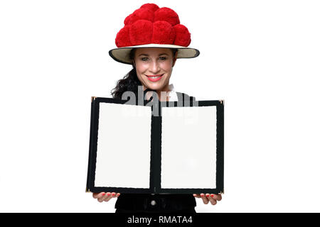 Pretty Black Forest waitress in a traditional Bollenhut with red pompoms holding open a blank menu with copy space with a friendly smile Stock Photo