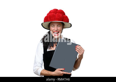 Candid portrait of a laughing attractive young Black Forest waitress holding a menu dressed in traditional clothes with a Bollenhut decorated with red Stock Photo