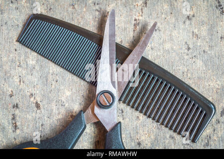 A scissors and a black comb kept on a grey wooden textured table top view. Stock Photo