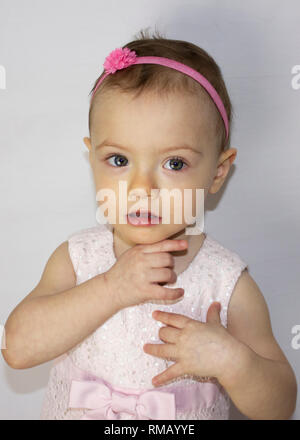 Very cute 20 months old baby portrait. Beautiful 1 year old toddler girl, posing naturally. Little girl, wearing cute pink dress and headband. Stock Photo