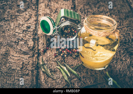 Olive oil flavored with lemon and peppercorns on wooden table, shabby style photo. Stock Photo