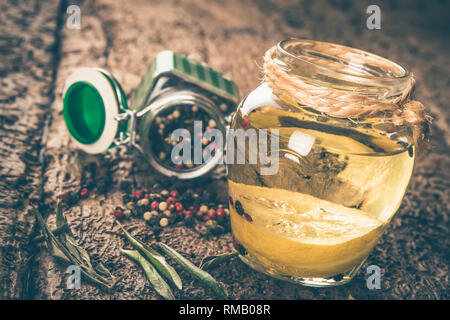 Olive oil flavored with lemon and peppercorns on wooden table, shabby style photo. Stock Photo