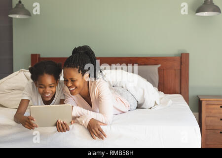 Happy African American mother and daughter lying on bed and using digital tablet Stock Photo
