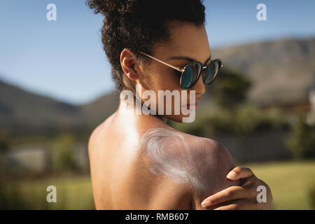 Young mixed-race woman rubbing sunscreen on shoulders