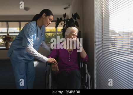 Female doctor consoling sad disable senior woman at nursing home Stock Photo