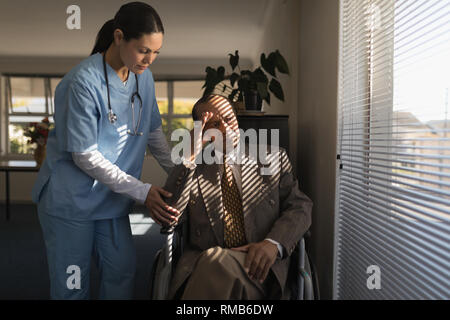 Female doctor consoling sad disable senior man at nursing home Stock Photo